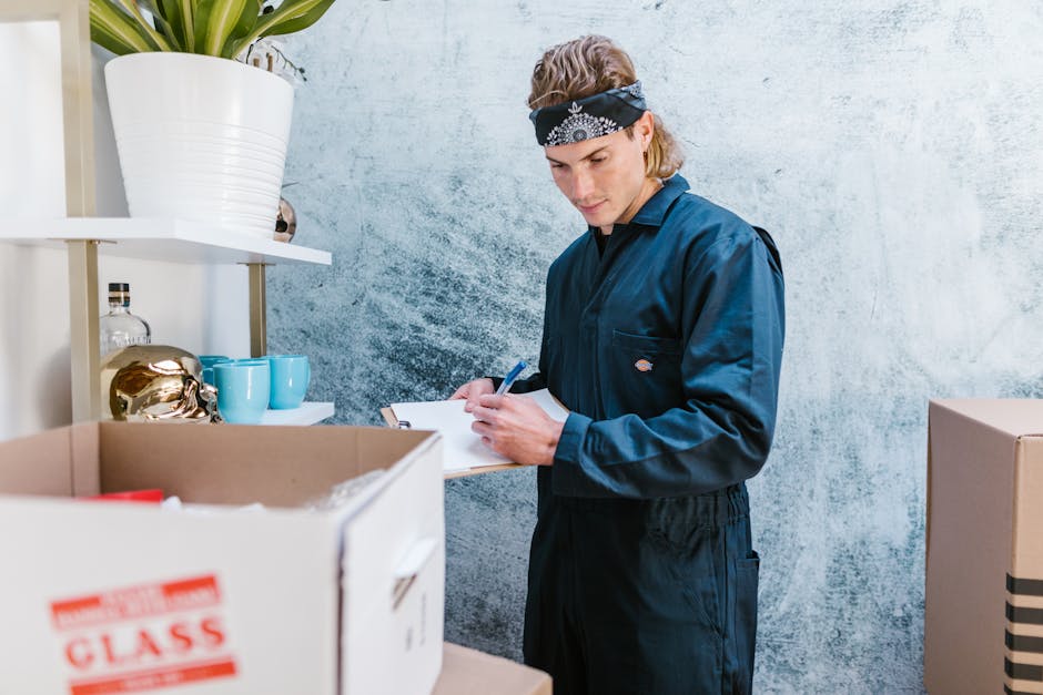 Two women are standing inside a property during a home relocation process, surrounded by various cardboard moving boxes sealed with red tape. One woman, with long dark hair and dressed in a checked sh